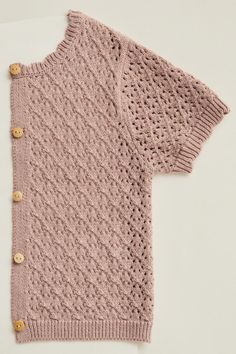 a pink knitted sweater with buttons on the front and back, sitting on top of a white surface