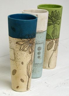 three different colored vases sitting next to each other on a white surface with leaves and flowers painted on them