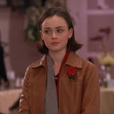 a woman wearing a brown leather jacket and gray scarf standing in front of a table