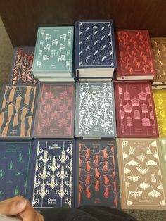 many different colored books sitting on top of a wooden table next to a person's hand