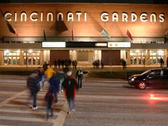 people crossing the street at night in front of a building that says cincinnati gardens on it