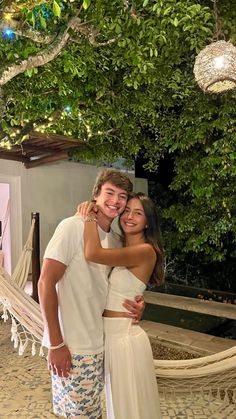 a man and woman standing next to each other in front of a hammock