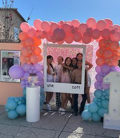 a group of people standing under a pink and blue arch with balloons on the side