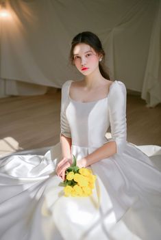 a woman sitting on the floor in a white dress with yellow flowers around her ankles