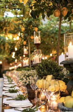 a long table with candles and lemons on it is set for an outdoor dinner