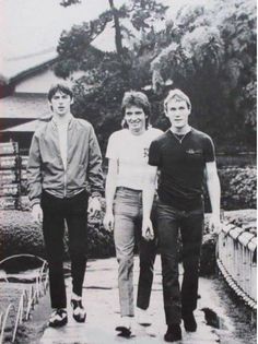 three people walking across a bridge in the middle of an outdoor area with trees and bushes behind them