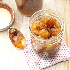 two jars filled with fruit sitting on top of a wooden table next to spoons