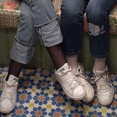 two people sitting on a bench with their legs crossed and one person wearing white sneakers