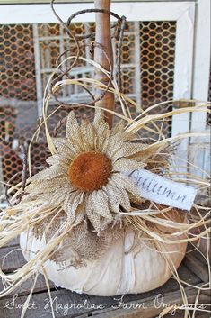 a white pumpkin decorated with a sunflower and some burlocks is sitting on a table