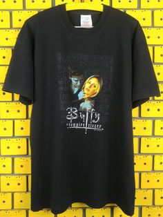 a black t - shirt hanging on a yellow brick wall with the image of two people