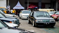 many cars are parked on the street in front of some tents and people walking around