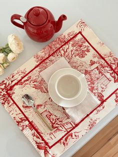 a red teapot sitting on top of a table next to a white plate and silverware