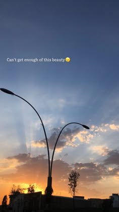 the sun is setting behind two street lamps and some clouds are in the sky above them