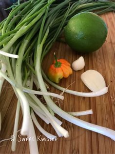 onions, green beans, and an orange are on a cutting board next to some scallions