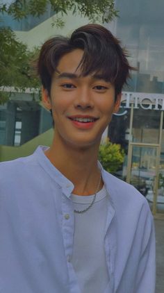 a young man standing in front of a building with a smile on his face and wearing a white shirt