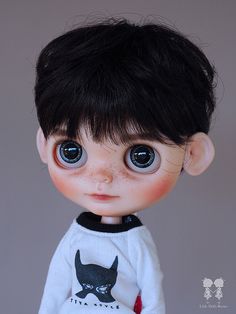 a close up of a doll with black hair and blue eyes wearing a white shirt