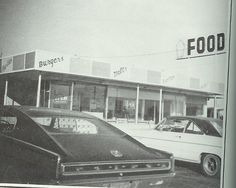 an old black and white photo of cars parked in front of a food store,