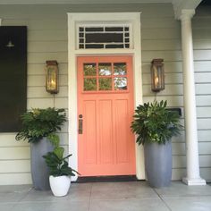 two large planters are on the front porch of a house with an orange door