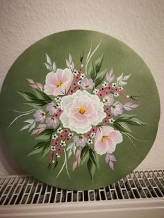 a green plate with pink and white flowers painted on the front is sitting on a shelf