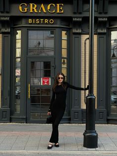 a woman standing next to a street light on the side of a road with her arms outstretched