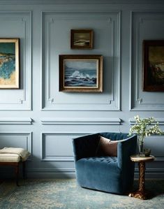 a blue chair in front of a wall with pictures on it and a vase filled with flowers