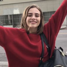 a woman in a red sweater is holding her arms up and smiling at the camera