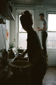 two people standing in a kitchen with pots and pans on the stove, talking