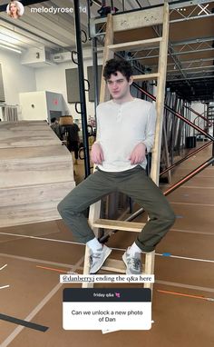 a young man sitting on top of a wooden ladder in an office building with stairs leading up to the ceiling