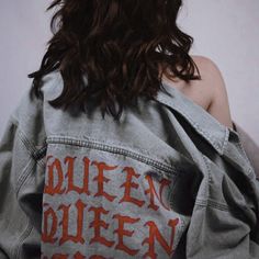 a woman wearing a jean jacket with the word queen written on it in orange ink