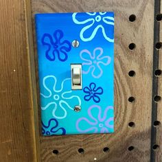 a light switch cover with blue and purple flowers painted on it, sitting on a wooden shelf