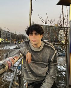 a young man sitting on top of a bench next to a metal railing with his arms crossed