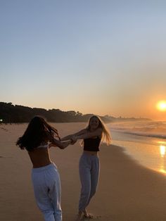 two women holding hands on the beach at sunset