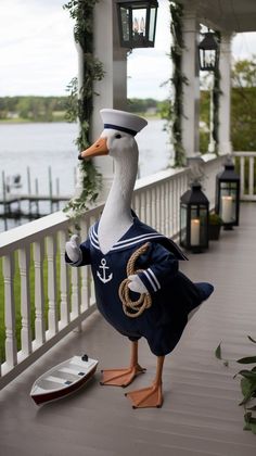 a statue of a duck dressed in a sailor's outfit on a porch next to a body of water