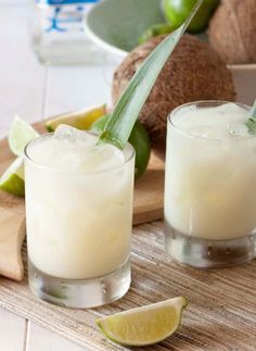 two glasses filled with ice and limes on a cutting board