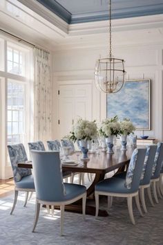 a dining room table with blue chairs and white vases on top of it in front of a large window