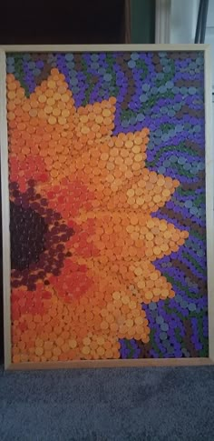 a painting made out of bottle caps with a sunflower in the middle and purple, orange, yellow and green colors