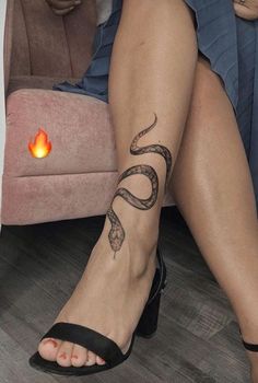 a woman's legs with a snake tattoo on her left leg, and a lit candle in the background