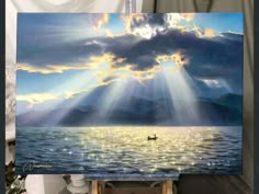 the painting is being displayed on easel in front of an easel with water and clouds