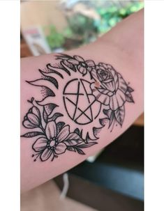 a black and white tattoo on the arm of a woman's arm with an inverted pentagramil surrounded by flowers