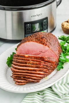 sliced ham on a white plate next to an instant pot roaster and parsley