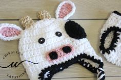 a crocheted cow hat and mittens are laying on a wooden surface,