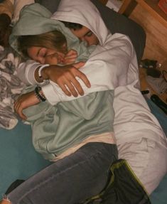 two people are laying on a bed and one person is hugging the other with their arms around each other