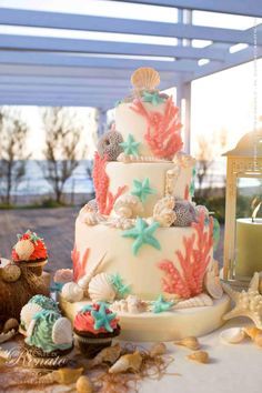 a wedding cake with seashells and starfish on the top is surrounded by shells