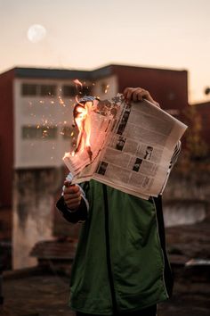 a man holding a newspaper with fire coming out of it's mouth and his face partially obscured by the paper