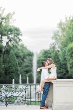 an engaged couple hugging in front of a fountain