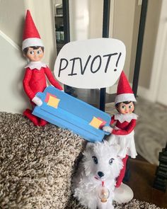 two elfs are holding a sign that says pivot and a white dog is sitting next to them