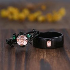 two wedding rings sitting on top of a wooden table next to each other with green and pink stones