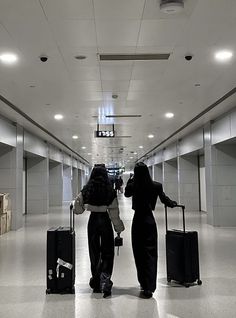 two women walking down an airport with their luggage