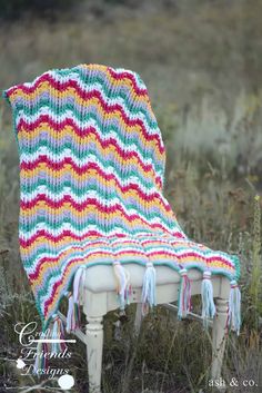 an old chair with a colorful blanket on it's back sitting in the grass