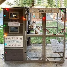 a chicken coop is decorated with christmas lights and signs on the outside, along with two cats